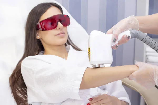 Laser hair removal and cosmetology. The girl removes hair on her arm with a laser. Cosmetology hair removal procedure. Laser hair removal and cosmetology. Cosmetology and SPA concept
