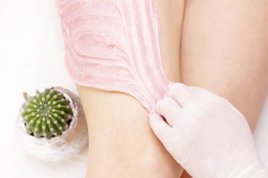Shugaring ustasının elleri genç bir kızın kalçalarına pembe shugaring macunu sürerler. Arka planda bir kaktüs var. tükürük konsepti. Güzellik salonu spa merkezi.
