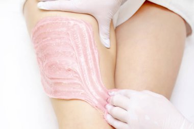 Shugaring ustasının elleri genç bir kızın kalçalarına pembe shugaring macunu sürerler. tükürük konsepti. Güzellik salonu spa merkezi.