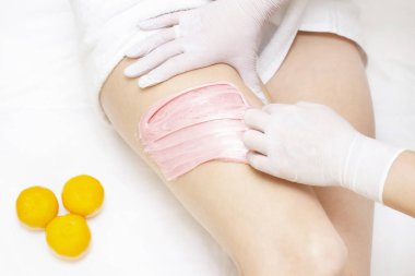 Shugaring ustasının elleri genç bir kızın kalçalarına pembe shugaring macunu sürerler. Arka planda bir mandalina var. tükürük konsepti. Güzellik salonu spa merkezi.