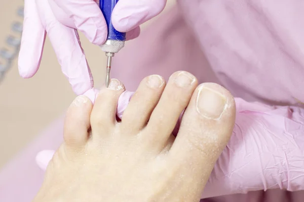 Professional hardware pedicure using an electric machine. Patient at the pedicure procedure. polishing the nail plate, processing the cuticle using a pedicure machine.