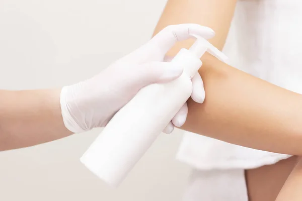 A young woman uses body cream. The girl holds in her hands a cream, gel, foam to moisturize the skin and applies it to the client. Cosmetology concept.