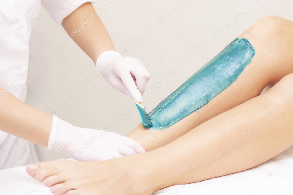 azulene depilation. wax hair removal, shugaring. concept of smooth skin without hair. azulene of green color. the master puts azulene on the girls legs