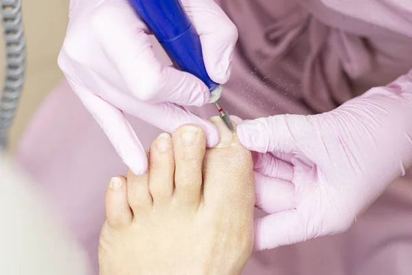 Professional hardware pedicure using an electric machine. Patient at the pedicure procedure. polishing the nail plate, processing the cuticle using a pedicure machine.