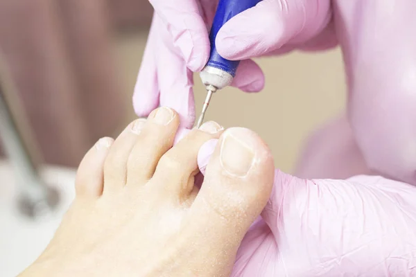 Professional hardware pedicure using an electric machine. Patient at the pedicure procedure. polishing the nail plate, processing the cuticle using a pedicure machine.