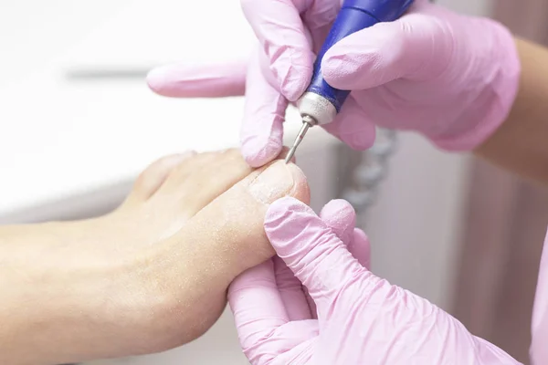 Professional hardware pedicure using an electric machine. Patient at the pedicure procedure. polishing the nail plate, processing the cuticle using a pedicure machine.