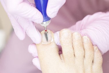 Elektrikli makine kullanan profesyonel donanım pedikürü. Pedikür prosedüründeki hasta. Tırnak kapağını cilalamak, ayak tırnağını pedikür makinesiyle işlemek..