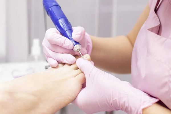 Professional hardware pedicure using an electric machine. Patient at the pedicure procedure. polishing the nail plate, processing the cuticle using a pedicure machine.