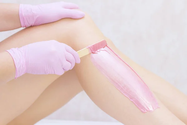Güzellik uzmanı, spa merkezinde pembe ağda yaptıran genç bir kadının bacakları ağda yapıyor. Tüylenme kavramı, pürüzsüz cilt.