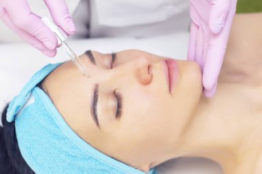 Doktor güzellik uzmanı prosedürü yapar, güzel bir kadının, kozmetoloji kliniğinin müşterisinin yüzüne vitamin serumu yerleştirir. Cilt bakımı kavramı