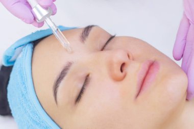 Doktor güzellik uzmanı prosedürü yapar, güzel bir kadının, kozmetoloji kliniğinin müşterisinin yüzüne vitamin serumu yerleştirir. Cilt bakımı kavramı