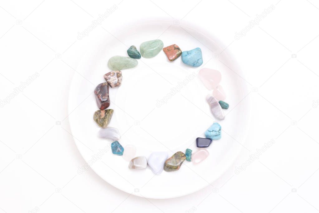 multi-colored stones on a white plate on a white background. place for your text, copy space. concept of witchcraft, fortune telling.