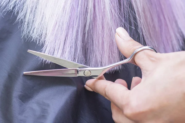 hairdresser makes haircut to a girl in with long blonde hair. Hairdresser hands holding scissors