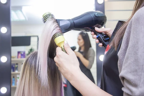 Making hairstyle using hair dryer. girl with blond long hair in a beauty salon. barbershop.