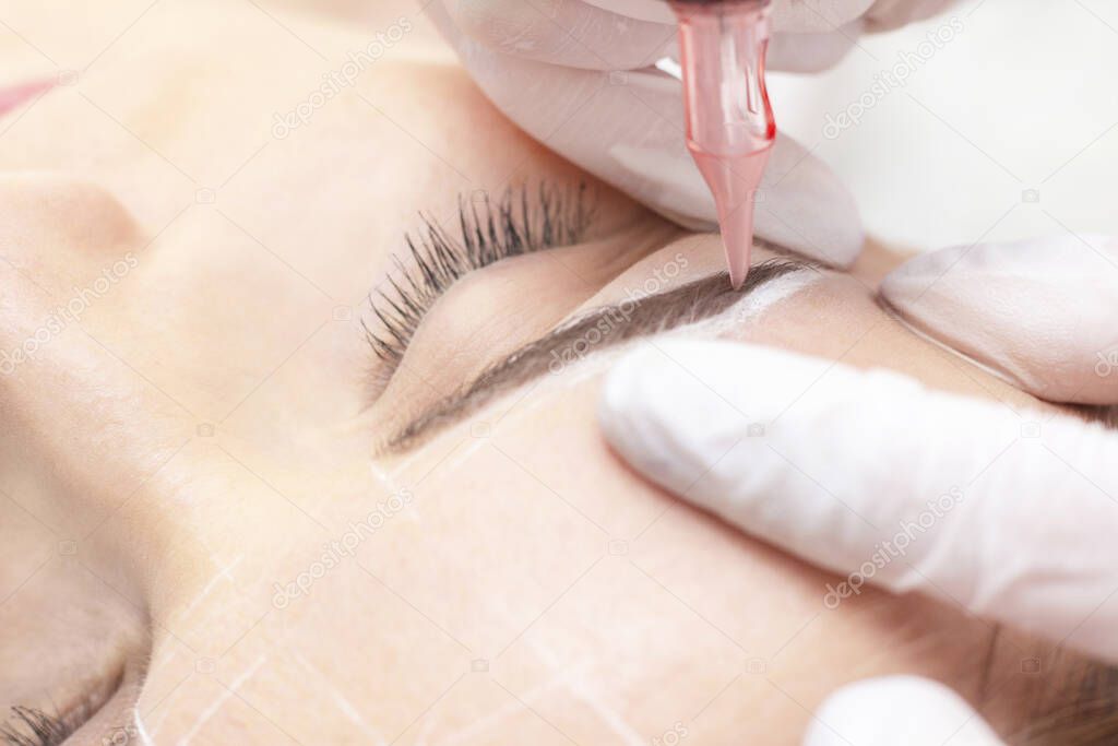 Make-Up. Beautician Hands Doing Eyebrow Tattoo On Woman Face.Permanent Brow Makeup In Beauty Salon. Close up Of Specialist Doing Eyebrow Tattooing For Female. Cosmetology Treatment.