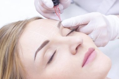 Bir güzellik salonunda kalıcı kaş makyajı yaptıran genç bir kadının yakın çekimi.