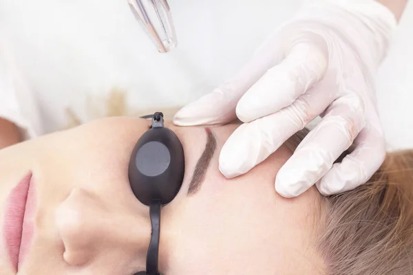 laser removal of permanent eyebrow makeup. A young woman undergoes laser removal of permanent makeup in a salon. Eyebrow correction