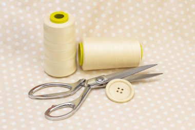 Bej pamuklu makaralar. Bej benekli kumaş üzerinde makas ve ahşap bir düğme. Doğal dikiş konsepti