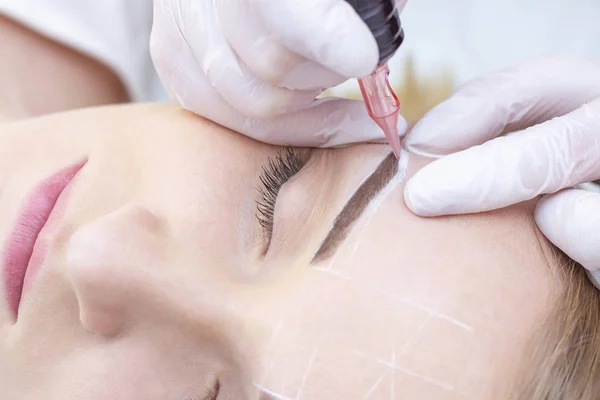 Close-up of a young woman undergoing permanent eyebrow makeup in a beauty salon