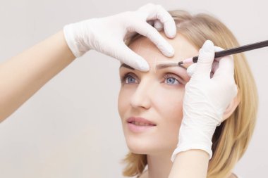 Makyaj malzemesi. Güzellik Uzmanı Elleri Kadın Yüzünde Kaş Dövmesi Yapıyor. Güzellik Salonunda Kalıcı Oral Makyaj. Dikey fotoğraf. Kozmetoloji Tedavisi.