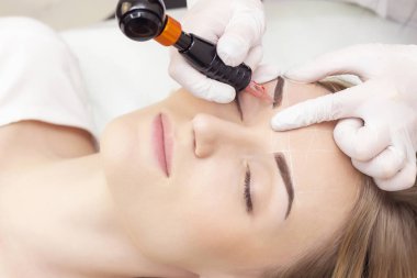 Makyaj malzemesi. Güzellik Uzmanı Elleri Kadın Yüzünde Kaş Dövmesi Yapıyor. Güzellik Salonunda Kalıcı Oral Makyaj. Dikey fotoğraf. Kozmetoloji Tedavisi.
