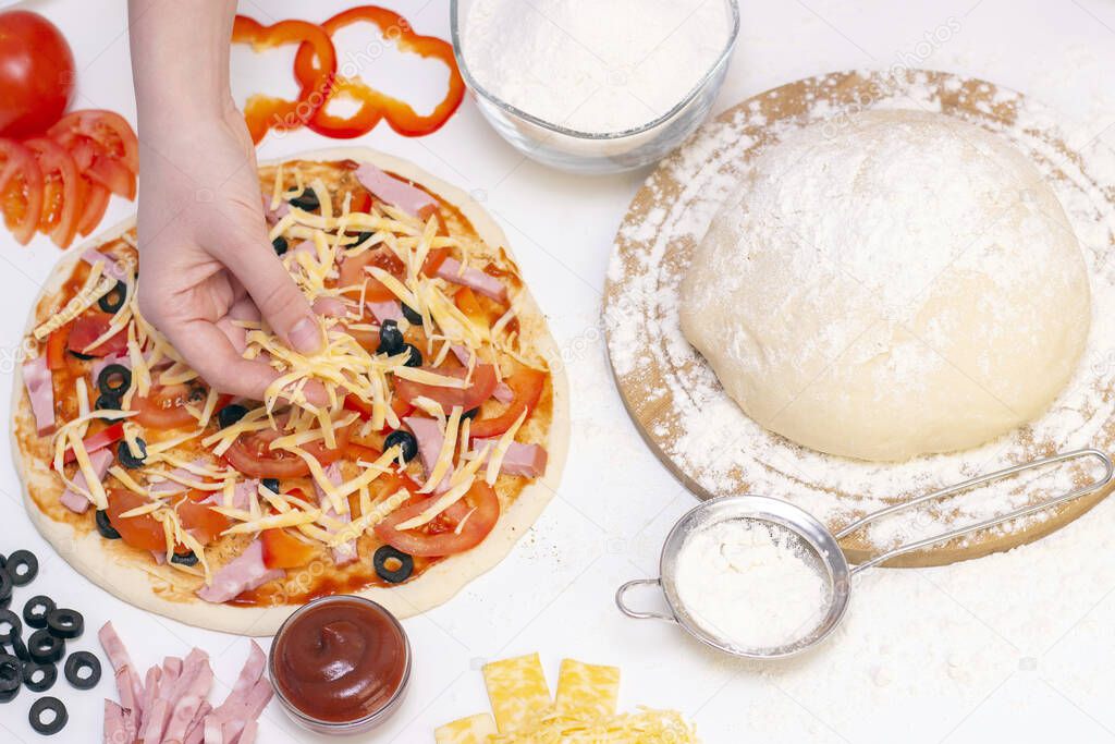 Ingredients for making pizza on a white background. Italian food. A cook sprinkles grated cheese on pizza. Cheese, tomato, pizza dough, flour, sauce, olives and others