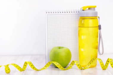 Yeşil elma, bir mezura, su şişesi ve tahta zemine yazmak için bir defter. Yaz sezonu ve plaj hazırlıkları, kilo kaybı ve spor konsepti