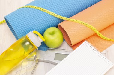 Ölçek, yeşil elma, mezura, defter, su şişesi ve tahta zeminde spor minderleri. kilo kaybı ve spor konsepti