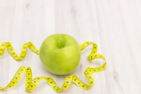 green apple, a measuring tape for writing on a light wooden background. preparation for the summer season and the beach, weight loss and sports concept