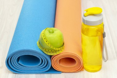 Yeşil elma, mezura, su şişesi ve tahta zeminde spor paspasları. kilo kaybı ve spor konsepti