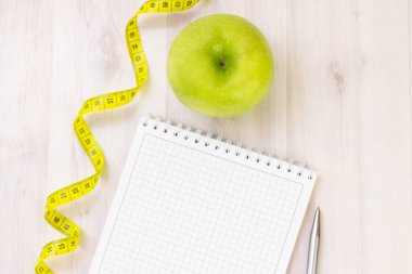 Yeşil elma, mezura, hafif ahşap arka planda defter. kilo kaybı ve spor konsepti