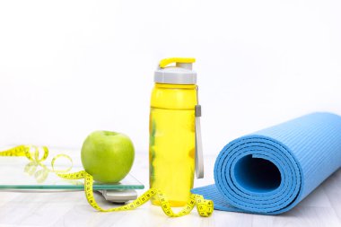 Ölçek, yeşil elma, mezura, su şişesi ve tahta zeminde spor minderleri. kilo kaybı ve spor konsepti