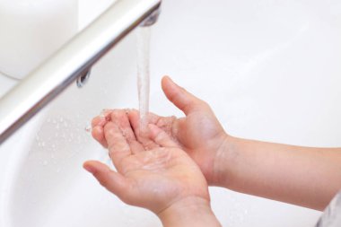 Çocukların elleri yıkanır. Antibakteriyel sabundan köpüklü çocuk elleri. Bakterilere ve koronavirüse karşı koruma. el hijyeni. Suyla el yıkama