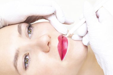 Güzellik salonunda dudaklarında kalıcı makyaj yapan genç bir kadın. Kalıcı Makyaj (Dövme) Beyaz bir dudak kalemiyle bir çizgi çizmek