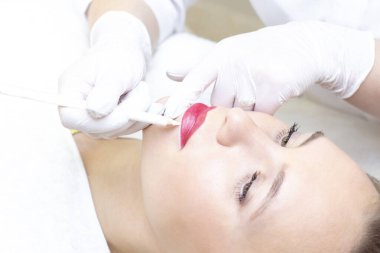 Güzellik salonunda dudaklarında kalıcı makyaj yapan genç bir kadın. Kalıcı Makyaj (Dövme) Beyaz bir dudak kalemiyle bir çizgi çizmek