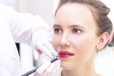 Güzellik salonunda dudaklarında kalıcı makyaj yapan genç bir kadın. Kalıcı Makyaj (Dövme) Beyaz bir dudak kalemiyle bir çizgi çizmek