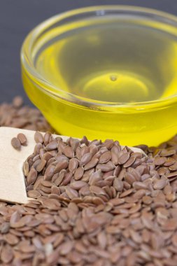 Ahşap bir kaşıkta siyah bir arka planda keten tohumu ve keten yağı yığını. Koyu renk keten tohumu kavramı. dikey resim