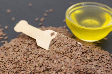 Ahşap bir kaşıkta siyah bir arka planda keten tohumu ve keten yağı yığını. koyu arkaplan keten tohumu kavramı.