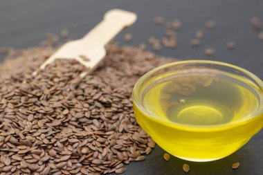 Ahşap bir kaşıkta siyah bir arka planda keten tohumu ve keten yağı yığını. koyu arkaplan keten tohumu kavramı.