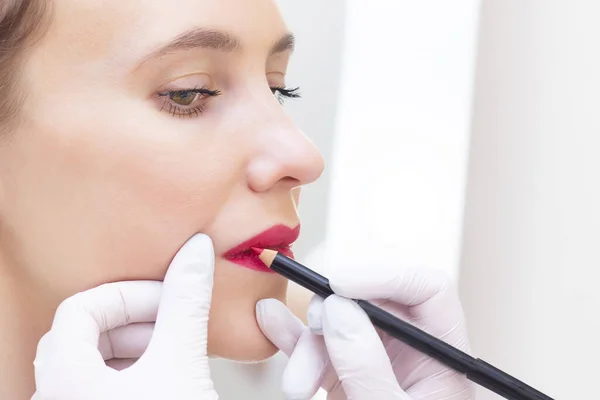 Young woman having permanent makeup on her lips at the beauticians salon. Permanent Makeup (Tattoo). drawing a contour with a white lip pencil