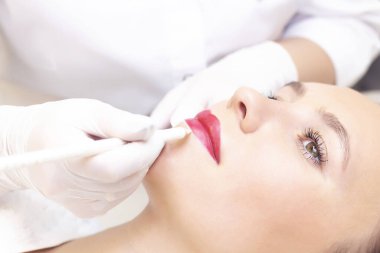 Güzellik salonunda dudaklarında kalıcı makyaj yapan genç bir kadın. Kalıcı Makyaj (Dövme) Beyaz bir dudak kalemiyle bir çizgi çizmek