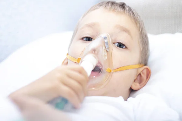 boy with an inhaler mask - respiratory problems in asthma. a boy with an inhaler mask lies in bed and breathes adrenaline. healthcare concept and sick child, coronavirus, bronchitis, pneumonia