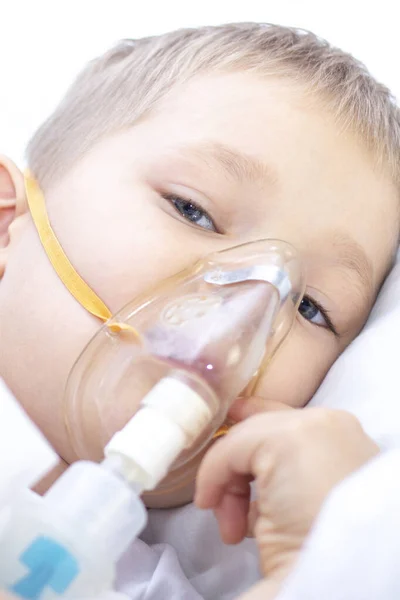 吸入マスクを持つ少年 喘息の呼吸器系の問題 吸入マスクの少年がベッドに横になってアドレナリンを吸う 医療の概念と病気の子供コロナウイルス気管支炎肺炎 垂直写真 — ストック写真