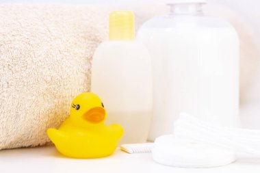 bebek hijyeni ve banyo malzemeleri, şampuan şişesi, bebek sabunu, havlu, sarı ördek lastik oyuncak, pamuk pedler ve tarak, tarak.