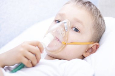 Astım maskeli bir çocuk. Astımda solunum problemleri var. Spreyli maskeli bir çocuk yatakta uzanıyor ve adrenalin soluyor. Sağlık konsepti ve hasta çocuk, koronavirüs, bronşit, zatürree