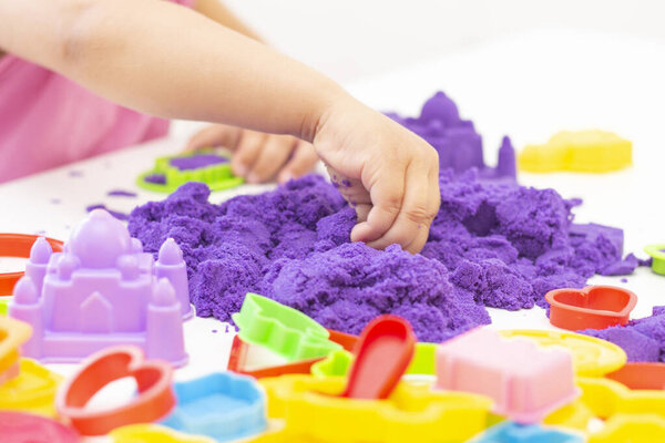 Childrens hands plays kinetic sand in quarantine. purple sand on a white table. coronavirus pandemic