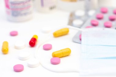 Birçok uyuşturucunun arka planında farklı renklerde haplar ve kapsüller ve koruyucu maske var. Sağlık, tedavi, hastalık kavramı.