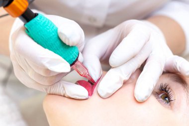 Güzellik salonunda dudaklarında kalıcı makyaj yapan genç bir kadın. Kalıcı Makyaj (Dövme) Beyaz bir dudak kalemiyle bir çizgi çizmek