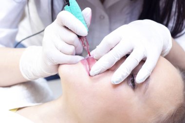 Güzellik salonunda dudaklarında kalıcı makyaj yapan genç bir kadın. Kalıcı Makyaj (Dövme) Beyaz bir dudak kalemiyle bir çizgi çizmek