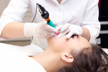 Güzellik salonunda dudaklarında kalıcı makyaj yapan genç bir kadın. Kalıcı Makyaj (Dövme) Beyaz bir dudak kalemiyle bir çizgi çizmek